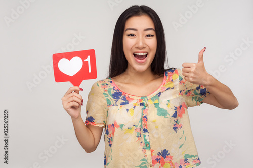 Put Like to social media content! Joyful enthusiastic asian girl showing internet heart icon and gesturing thumb up, recommending to subscribe and follow interesting blog. indoor studio shot, isolated photo