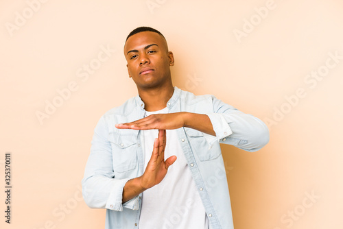 Young latin man isolated on beige background showing a timeout gesture.
