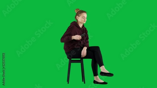 Young Girl Wearing a Sweatshirt Calling Someone While Sitting on Green Screen