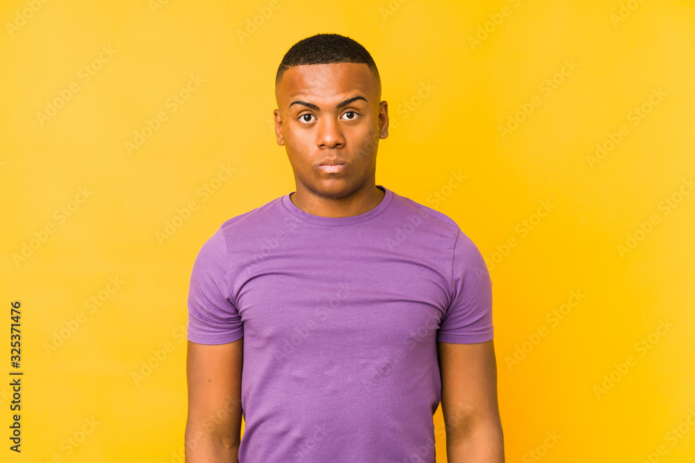 Young latin man isolated on yellow background shrugs shoulders and open eyes confused. Young latin man isolated on yellow background shrugs shoulders and open eyes confused.