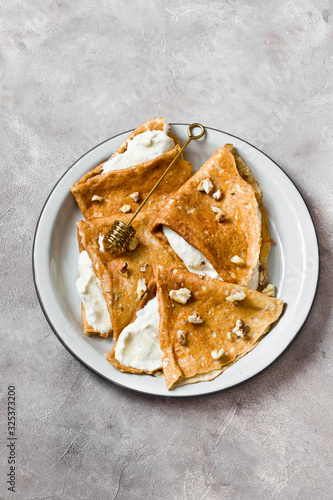 Crepes or thin pancakes with cottage cheese cream, honey and walnut. Traditional Maslenitsa (Shrovetide) meal and tasty breakfast on gray background. Copy space, top view.