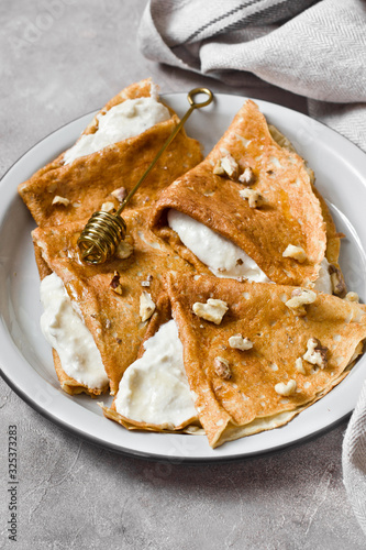 Crepes or thin pancakes with cottage cheese cream, honey and walnut. Traditional Maslenitsa (Shrovetide) meal and tasty breakfast on gray background.