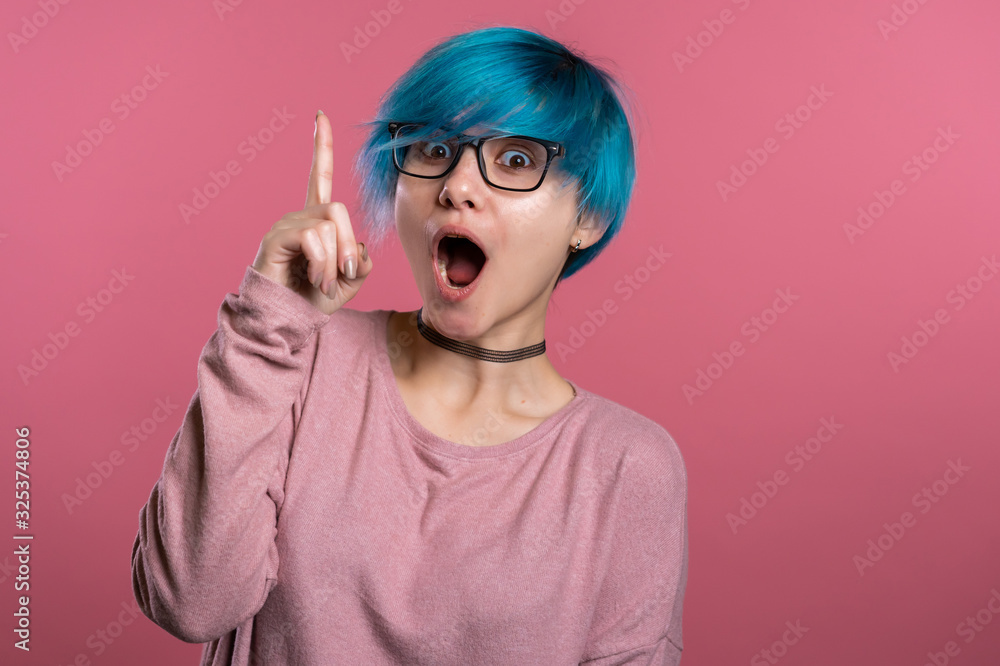 Portrait of young thinking pondering woman with unusual blue hairstyle having idea moment pointing finger up on pink studio background. Smiling happy girl showing eureka gesture. - obrazy, fototapety, plakaty 