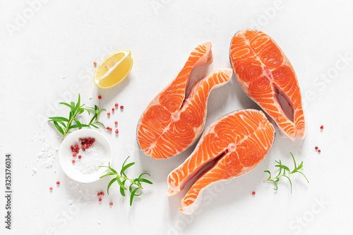 Salmon. Fresh raw salmon fish steaks with cooking ingredients, herbs and lemon on white background, top view