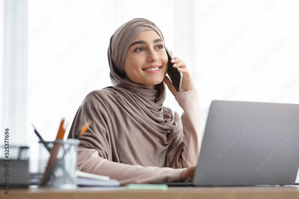 Arabic businesswoman talking on mobile phone while using laptop in office Arabic businesswoman talking on mobile phone while using laptop in office