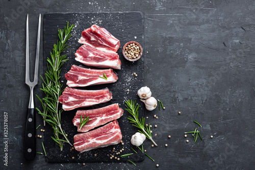 Fresh raw meat, pork ribs with cooking ingredients on black background with copy space, top view