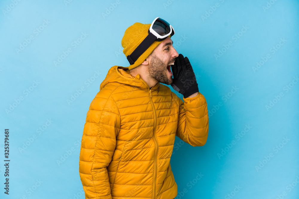 Young skier caucasian man isolated shouting and holding palm near opened mouth.