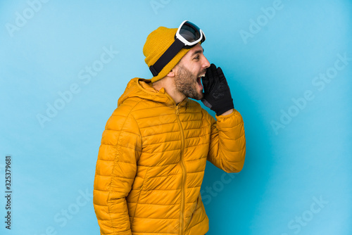 Young skier caucasian man isolated shouting and holding palm near opened mouth.