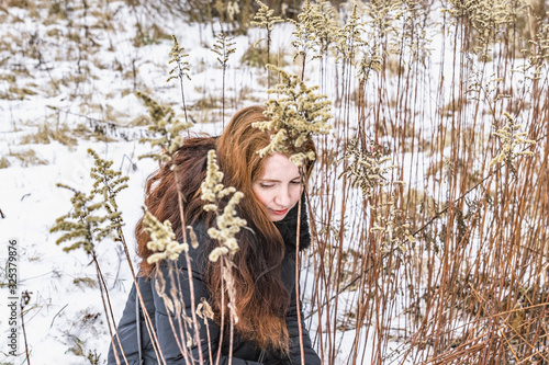 The girl sits in the dried tall grass with her hair loose and looks a little down.