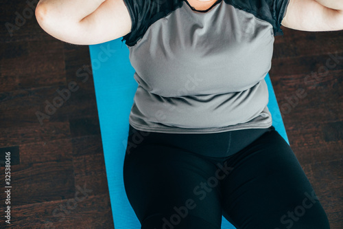 Fitness, weight loss, home workout. Overweight woman doing sit-ups on mat indoors photo