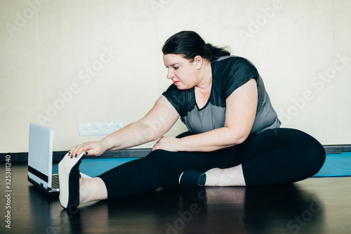 Overweight woman stretching while watching online workout indoors. Exercising at home. Internet fitness class or video course