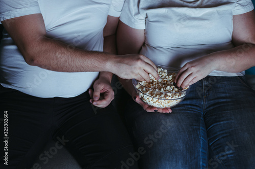 Emotional eating, nerve food, laziness. Overweight couple watching tv eating junk food late in the night