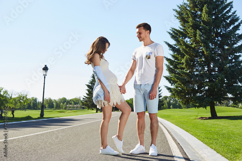 Happy couple in love waiting for child pregnancy hug walk in the summer park green trees nature husband and wife baby boy young family parent, man woman romantic dating harmony relationship.