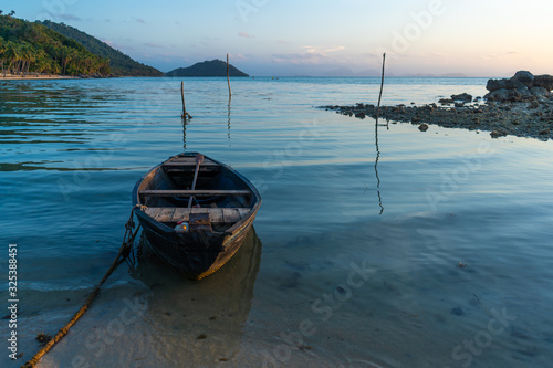 Wooden boat off the coast of a tropical island. Evening, sunset in the ocean. Tropical landscape. Light waves rock the boat