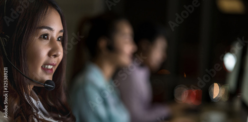 Portrait of Asian Female customer care service with business man smiling and working hard late in night shift at office,call center department,worker and overtime,teamwork with colleagues for success