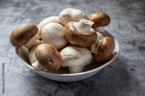 Close-up of white and brown mushrooms, in a white ceramic bowl, on a gray concrete surface