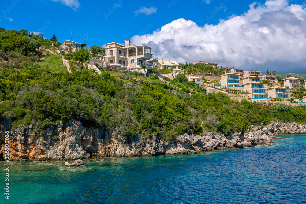 New villas and houses on the cliff over the sea with rocks in turquoise water. Summer landscape- green trees and blue sky. 