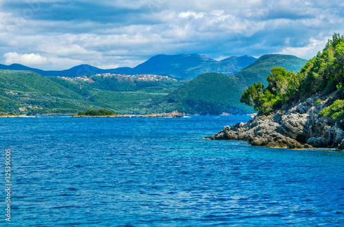 Beautiful summer landscape with sea lagoon, rocks and cliffs, green trees on the coast, mountains on the horizon and clouds on the sky. 