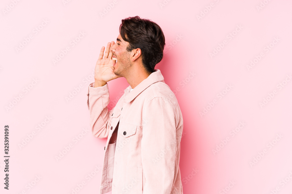 Young caucasian man posing in a pink background isolated shouting and holding palm near opened mouth. Young caucasian man posing in a pink background isolated shouting and holding palm near opened mouth.