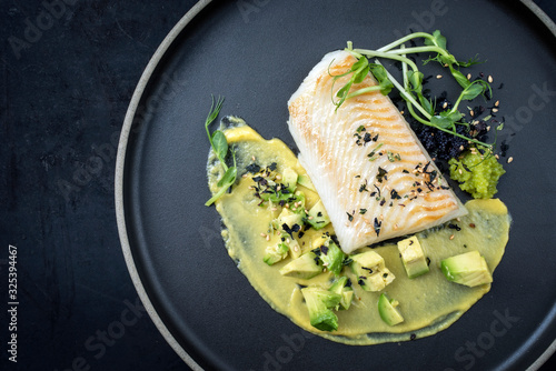 Gourmet Kabeljau Fisch Filet gebraten mit Kaviar, Avocado Scheiben und Mango Senf Creme als Draufsicht auf einem Modern Design Teller mit Textfreiraum links photo