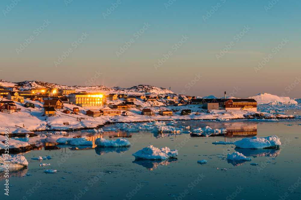Glacier-filled waters and a snowy artic village at sunset, Greenland.