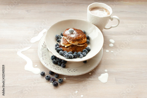 Low Carb Keto Diet Pancakes from almond coconut flour with blueberries, cream on white plate and cocoa cup on wooden table background close up view. Selective focus. Copy space. Ketogenic concept