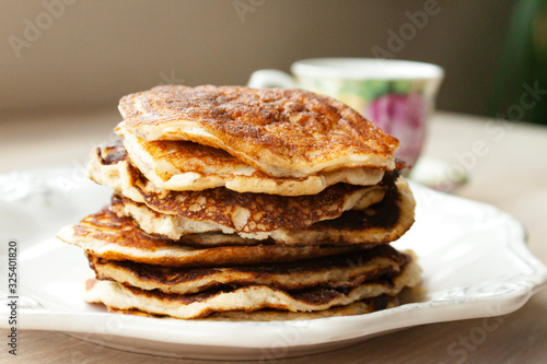 Low Carb Keto Diet Pancakes from almond coconut flour stack on white plate and cup of cocoa on wooden table background close up view. Selective focus. Copy space. Ketogenic concept