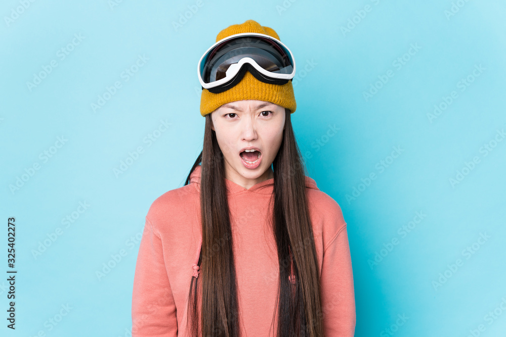 Young chinese woman wearing ski clothes isolated screaming very angry and aggressive. Young chinese woman wearing ski clothes isolated screaming very angry and aggressive.
