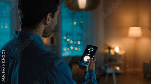 Fotografie Young Handsome Man is Holding Smartphone with Active Smart Home Application