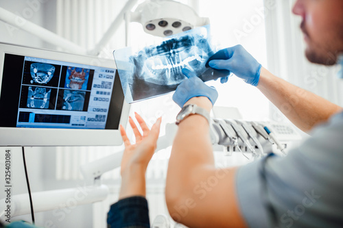 Medicine, dentistry and healthcare concept, dentist showing teeth x-ray to female patient at dental clinic office.