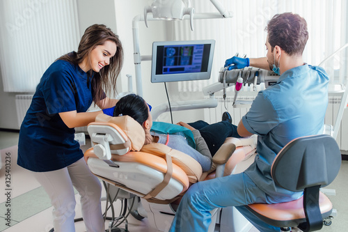 Tableau sur toile Young dentist in latex blue gloves is examining woman teeth with a help of a dental probe and a mirror