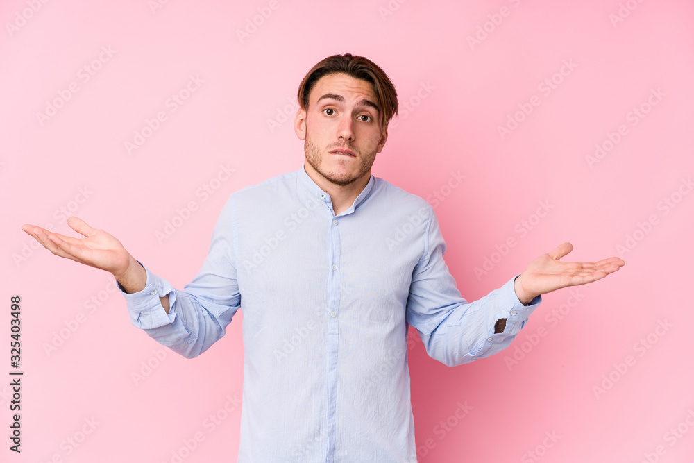 Young caucasian man posing in a pink background isolated confused and doubtful shrugging shoulders to hold a copy space. Young caucasian man posing in a pink background isolated confused and doubtful shrugging shoulders to hold a copy space.