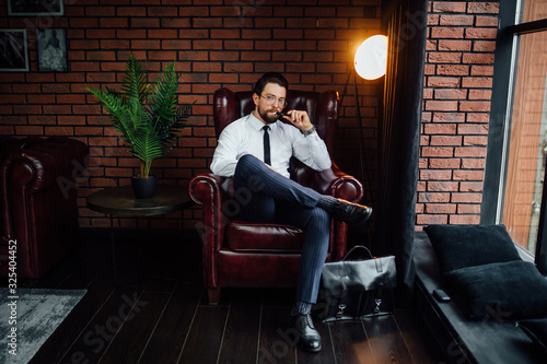 Millionaire man resting and relaxing while sitting on sofa in luxury room. Handsome man smoking cigar or iqos. photo