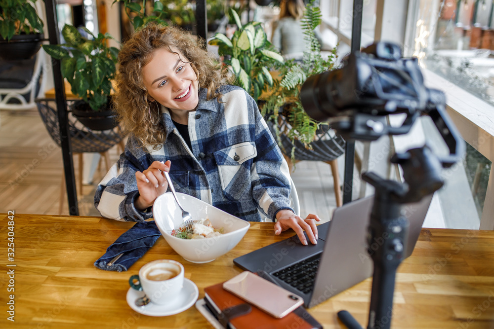 Portrait of young woman in casual wear speak to the camera in modern cafe terrace with cup of coffee and salade