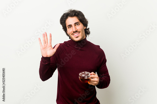 Young man holding a tea cup smiling cheerful showing number five with fingers.