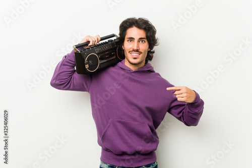 Young urban man holding a guetto blaster person pointing by hand to a shirt copy space, proud and confident