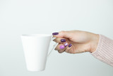 Dłonie kobiety trzymające kubek z kawą, na jasnym tle
