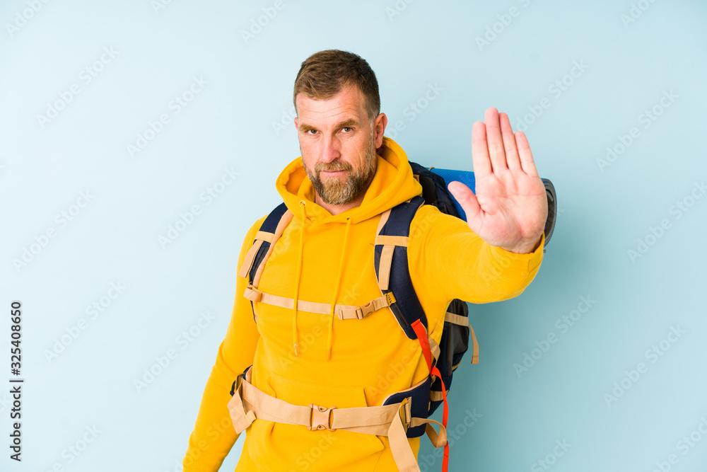 Senior hiker man isolated on blue background standing with outstretched hand showing stop sign, preventing you. Senior hiker man isolated on blue background standing with outstretched hand showing stop sign, preventing you.