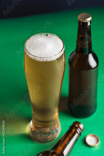 Two dark beer bottles, a glass of beer and foam on a green and blue background.