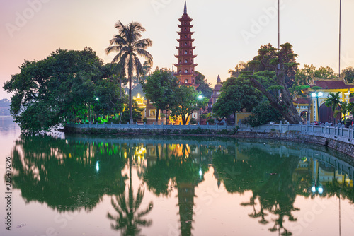 Hanoi buddhist pagoda (Tran Quoc Pagoda) on West Lake at Hanoi, colorful sunset, illuminated temple, water reflection. Vietnam travel.