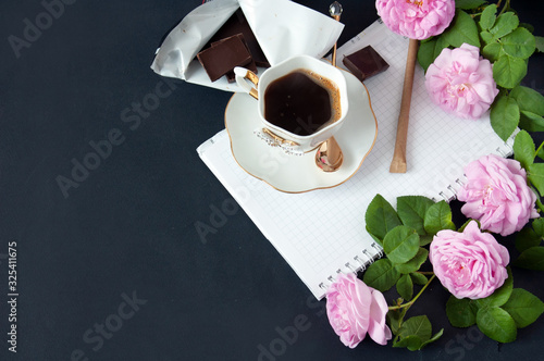 Cup of coffee, roses bunch, notepad, pen, chocoate and phone on black background photo