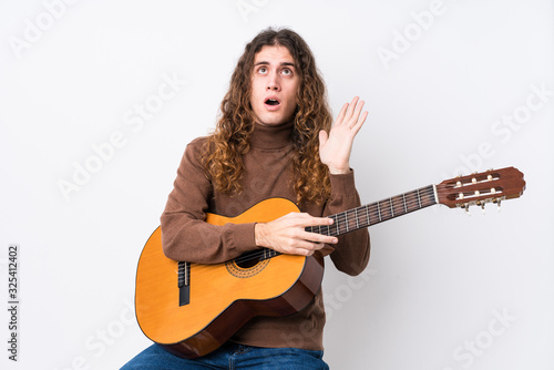 Young caucasian man playing guitar isolated surprised and shocked.