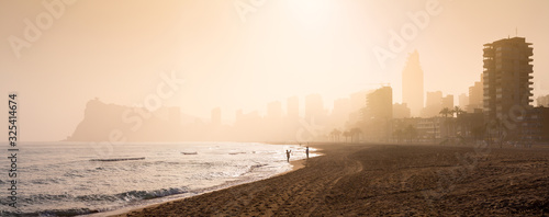 Wonderful romantic panoramic seascape of summer resort. People relaxing on the beach in a shine bright light through foggy breese. Costa Blanca. City of Benidorm, Alicante, Valencia, Spain.