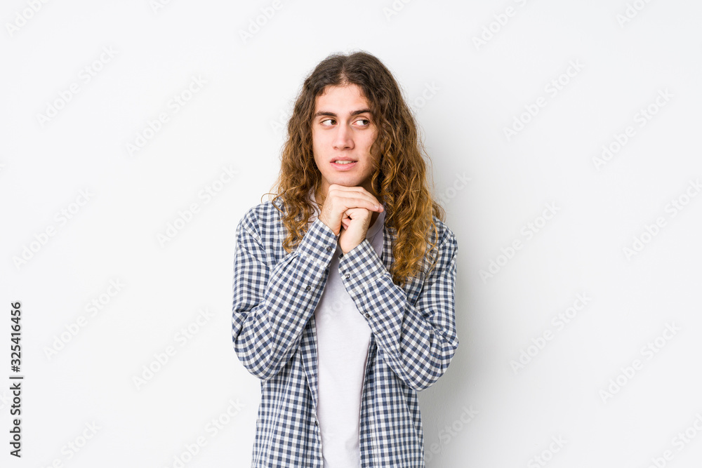 Young long hair man posing isolated keeps hands under chin, is looking happily aside. Young long hair man posing isolated keeps hands under chin, is looking happily aside.