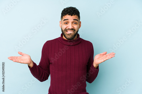 Young mixed race arabic man isolated confused and doubtful shrugging shoulders to hold a copy space.