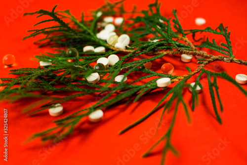 Spruce branch with pills scattered on it, drugs close-up on a red background.  Medical concept.  Pharmacist