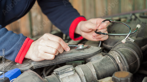 closeup of man's hand with stethoscope checking car engine, auto service concept
