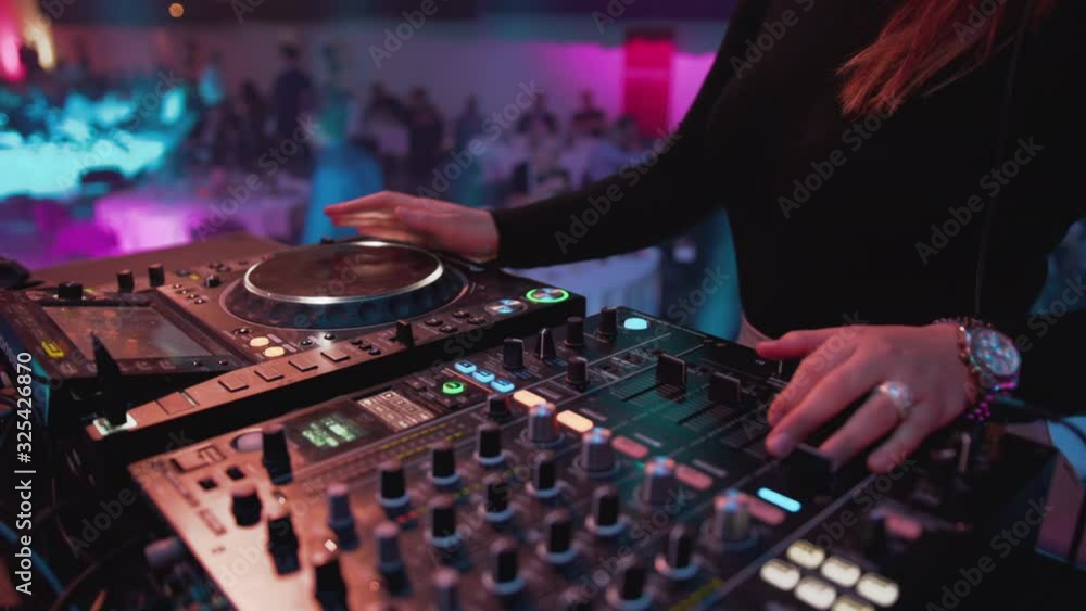 White female DJ controls digital deck, presses buttons and turns a turntable, slow pan out White female DJ controls digital deck, presses buttons and turns a turntable, slow pan out