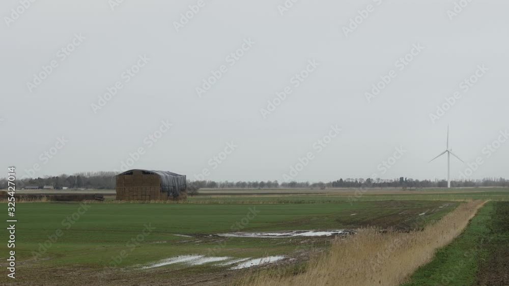 A wind turbine and haystack in the countryside with a flooded field. STATIC SHOT. A wind turbine and haystack in the countryside with a flooded field. STATIC SHOT.