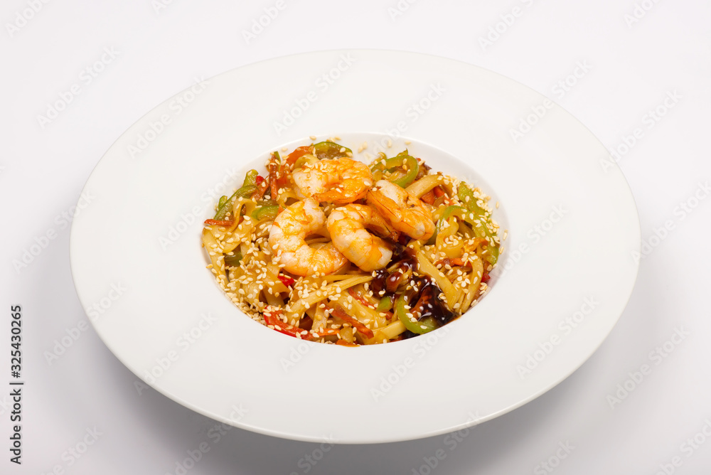 Asian style wheat noodles with shrimp, sweet peppers, sesame seeds and soy sauce in a white plate on a white background Asian style wheat noodles with shrimp, sweet peppers, sesame seeds and soy sauce in a white plate on a white background